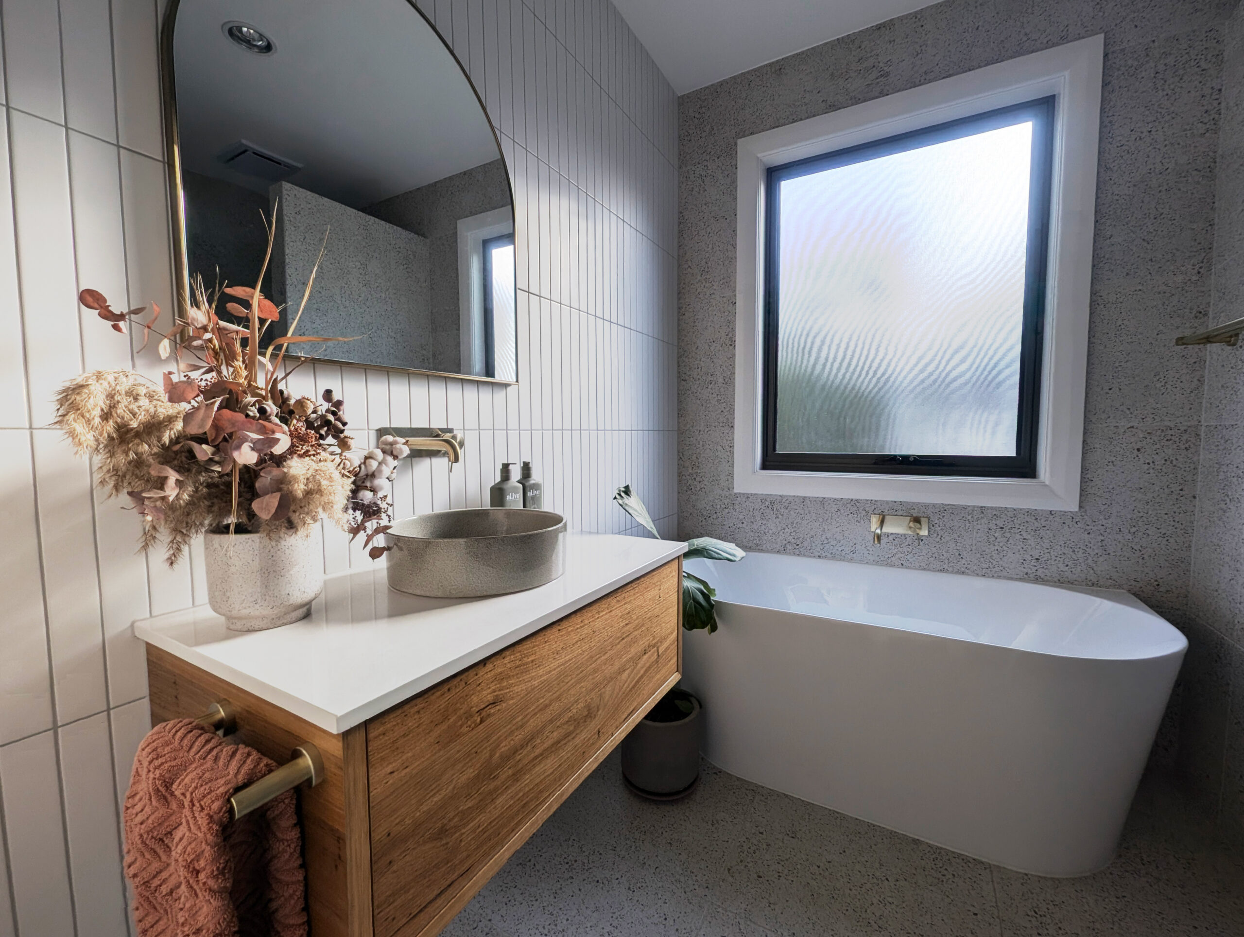 The Balhannah bathroom in full — floating vanity, freestanding bath and brass tapware over heated terrazzo-look floors