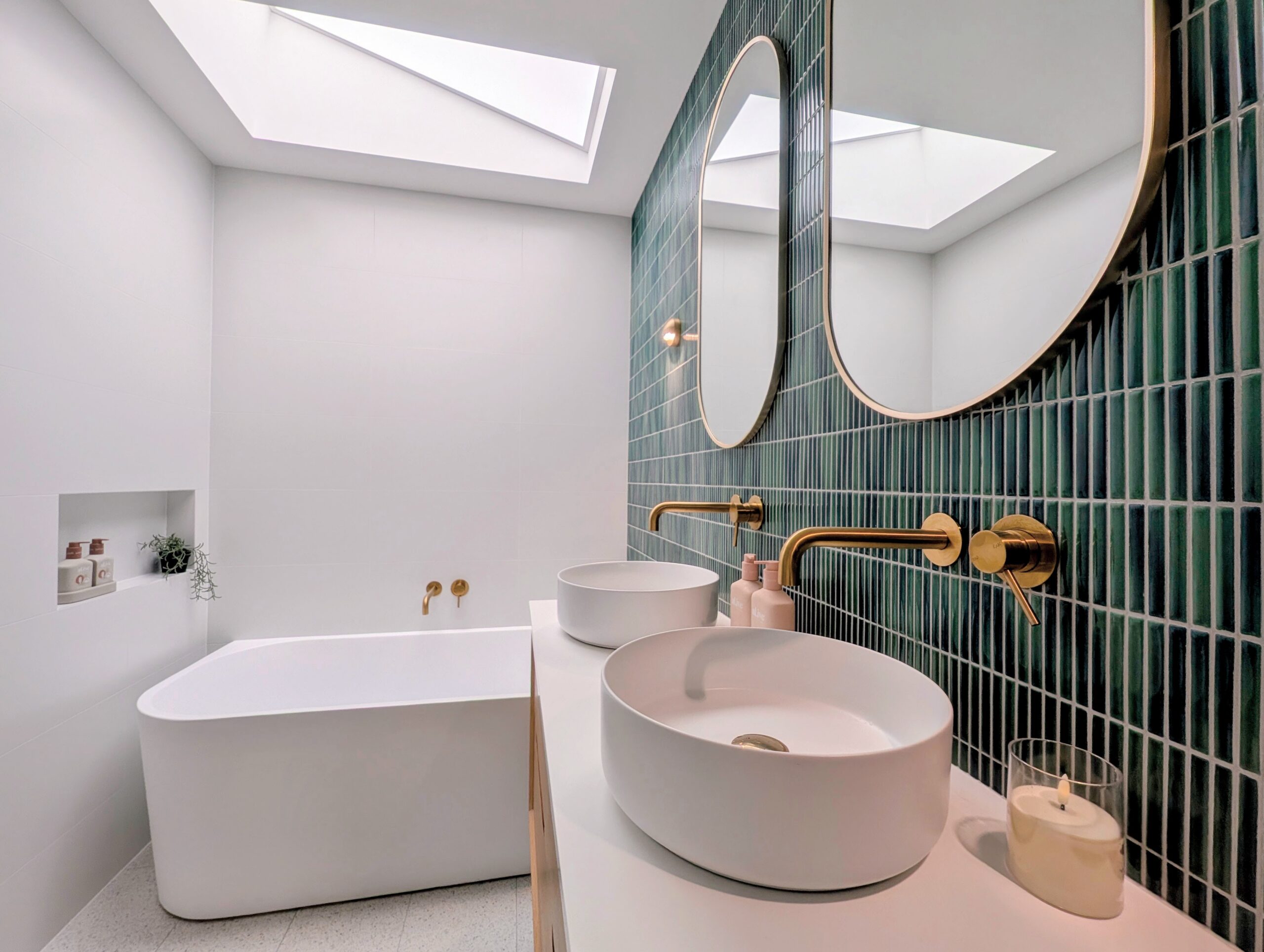 Skylight filling the bathroom with light, showing the lush green Kit Kat tiles and brass tapware above the vanity