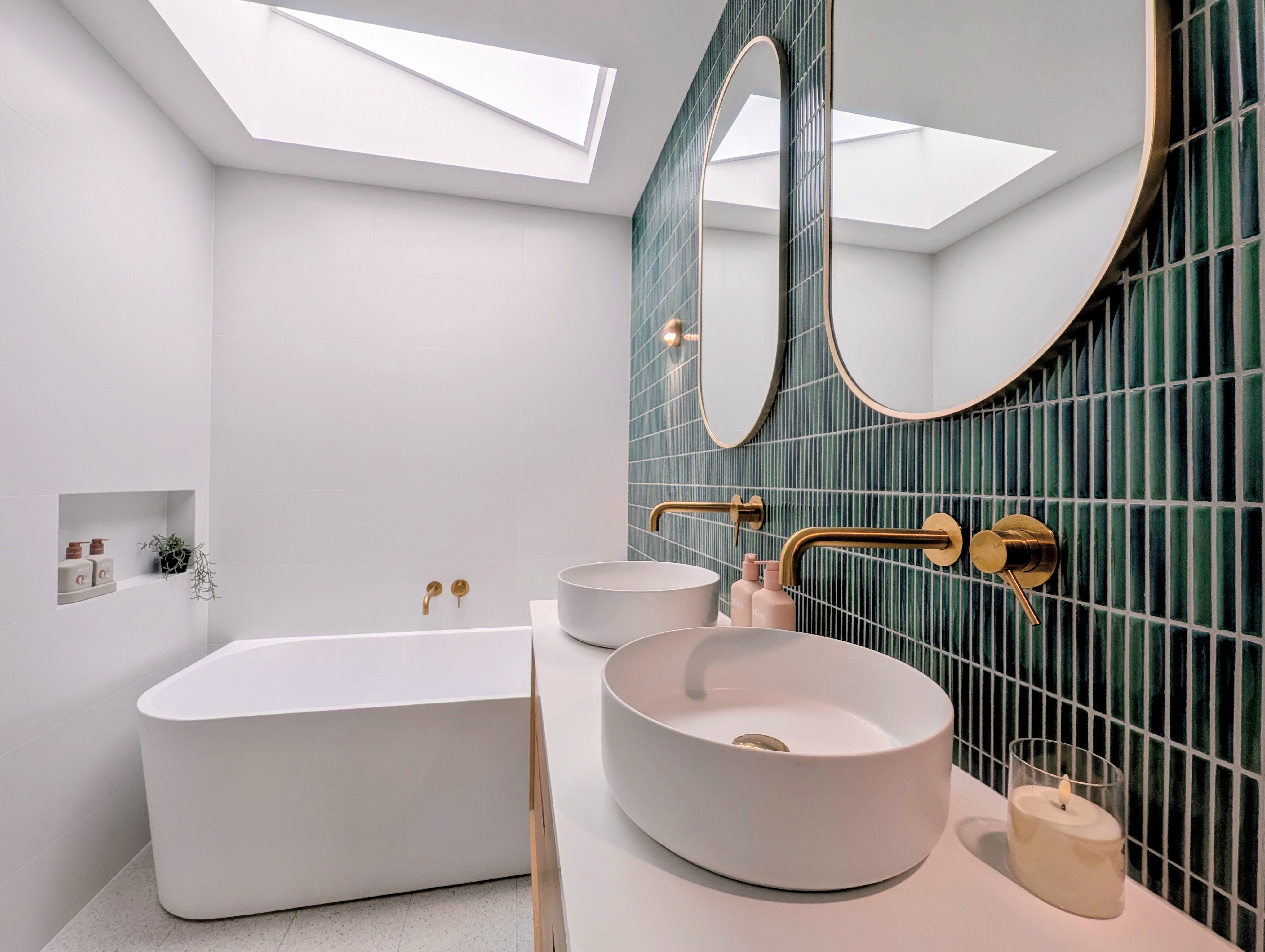 Skylight filling the bathroom with light, showing the lush green Kit Kat tiles and brass tapware above the vanity