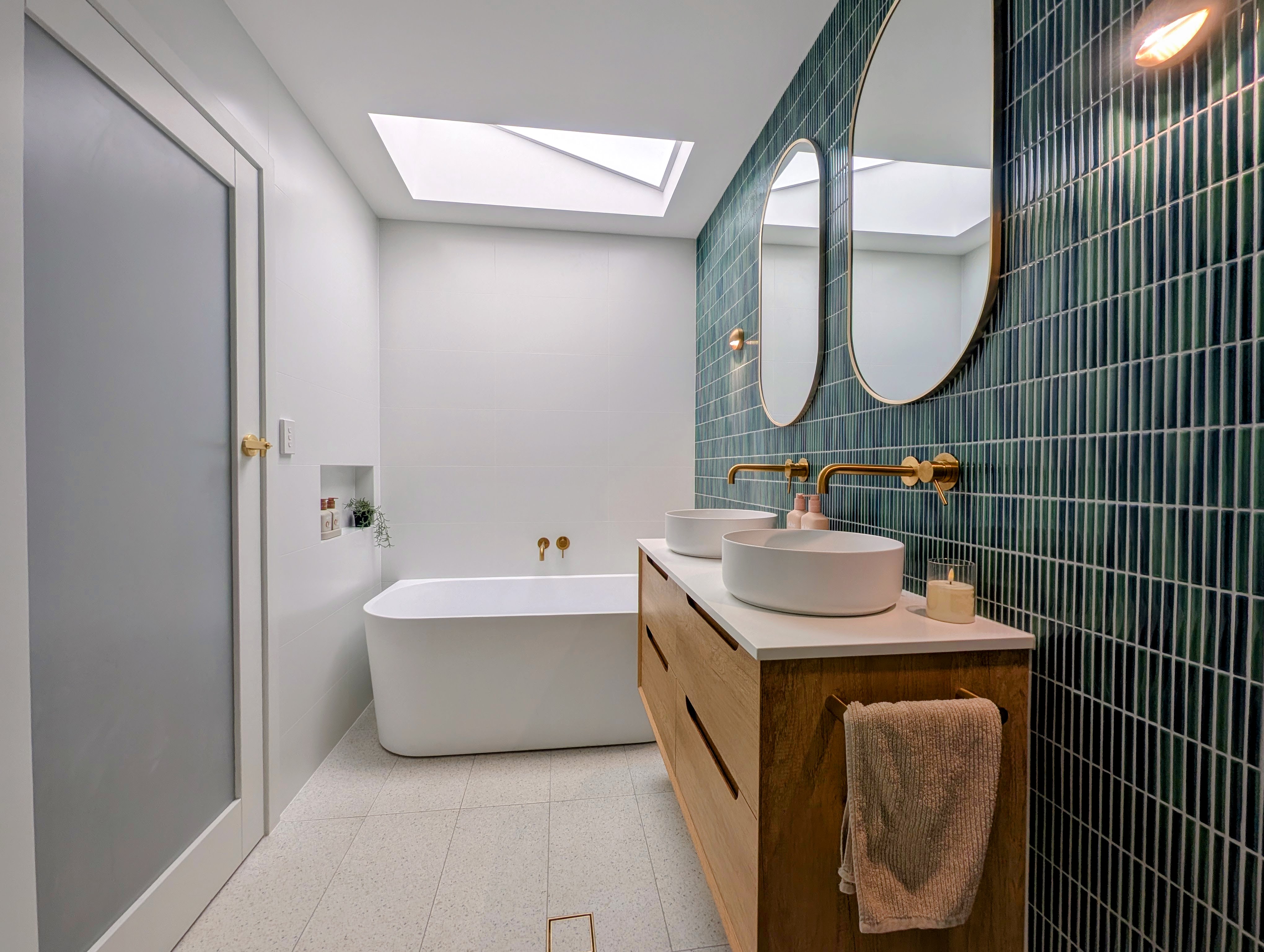 The finished Lobethal bathroom — freestanding bath against the green Kit Kat tile feature wall, double vanity with brass tapware and daylight from the skylight overhead