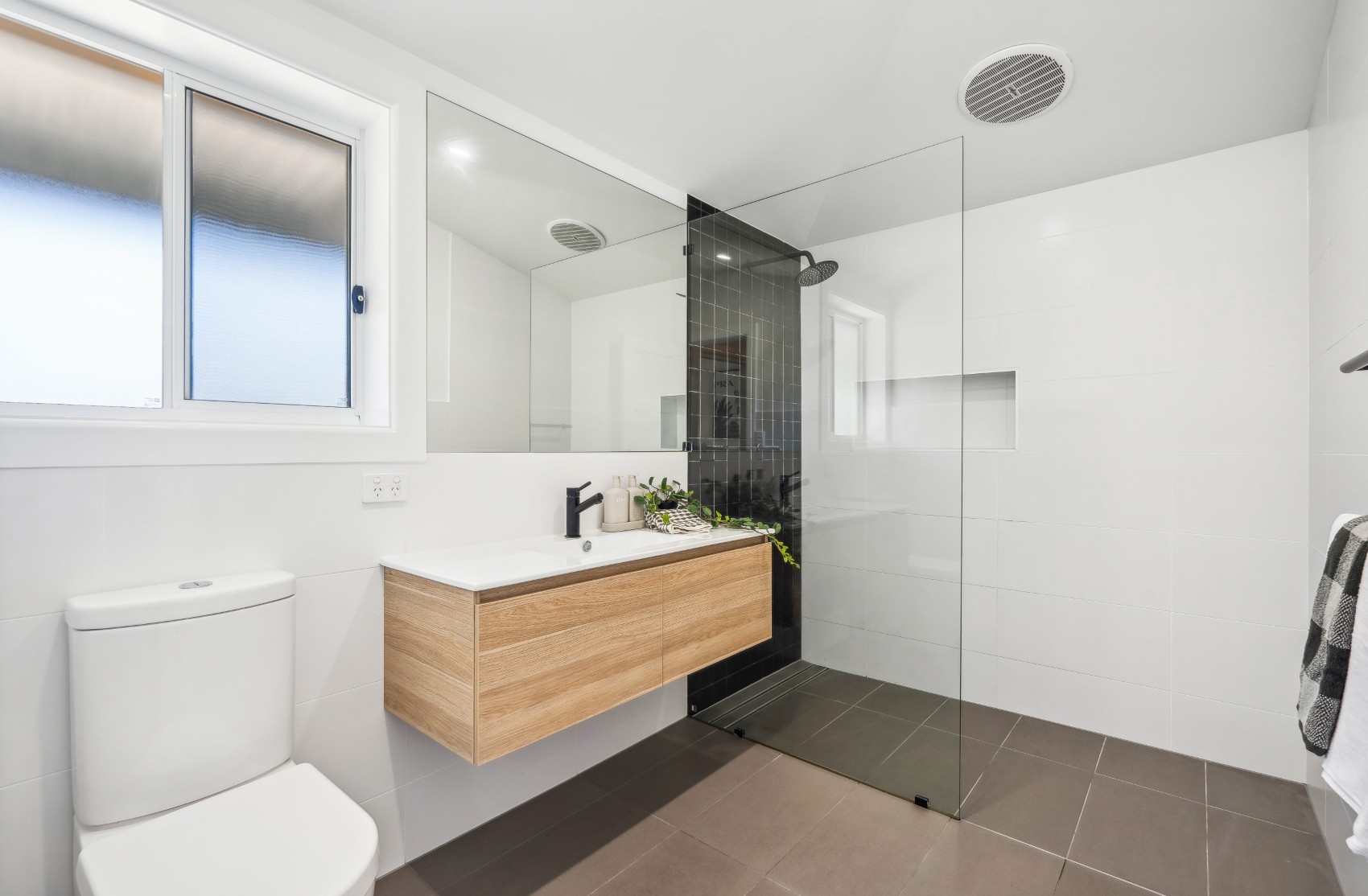 Renovated Charleston bathroom — floating timber vanity and black-tiled shower behind frameless glass
