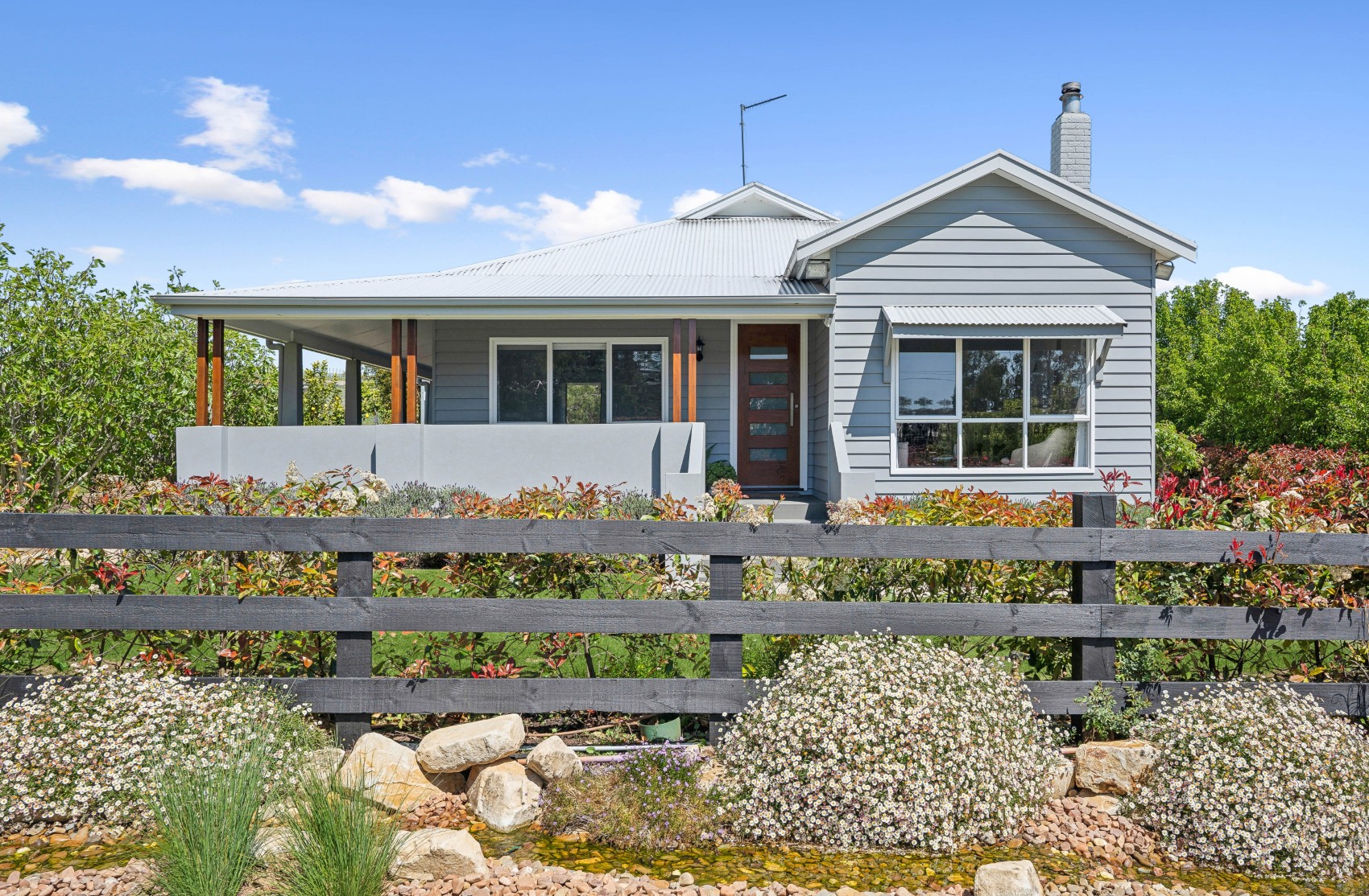 Renovated Charleston home from the street — grey weatherboard with wraparound verandah on timber posts, behind the post-and-rail fence and cottage garden