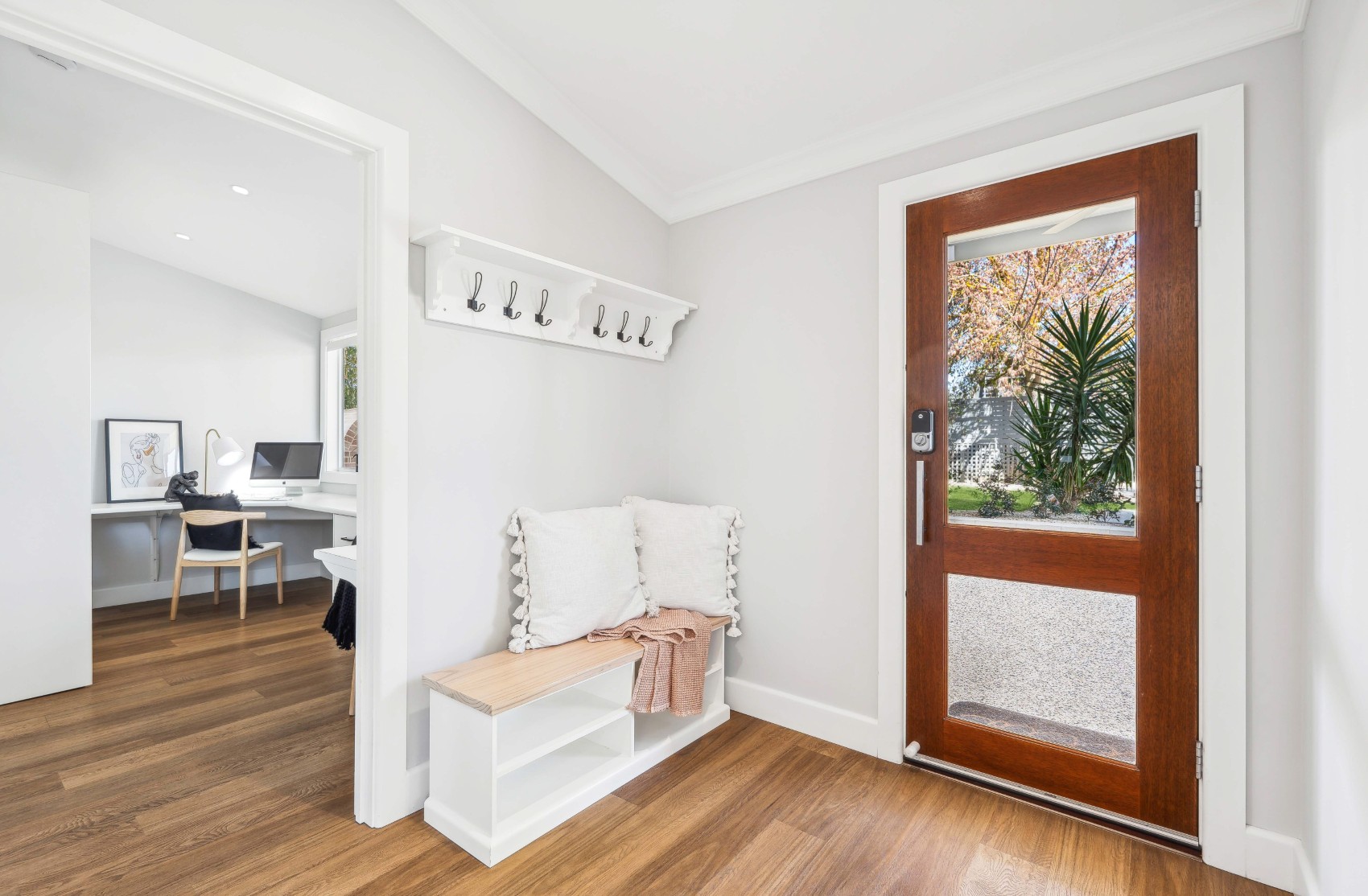 Entry of the renovated Charleston home \u2014 bench seat and coat hooks beside the timber-and-glass front door, home office beyond