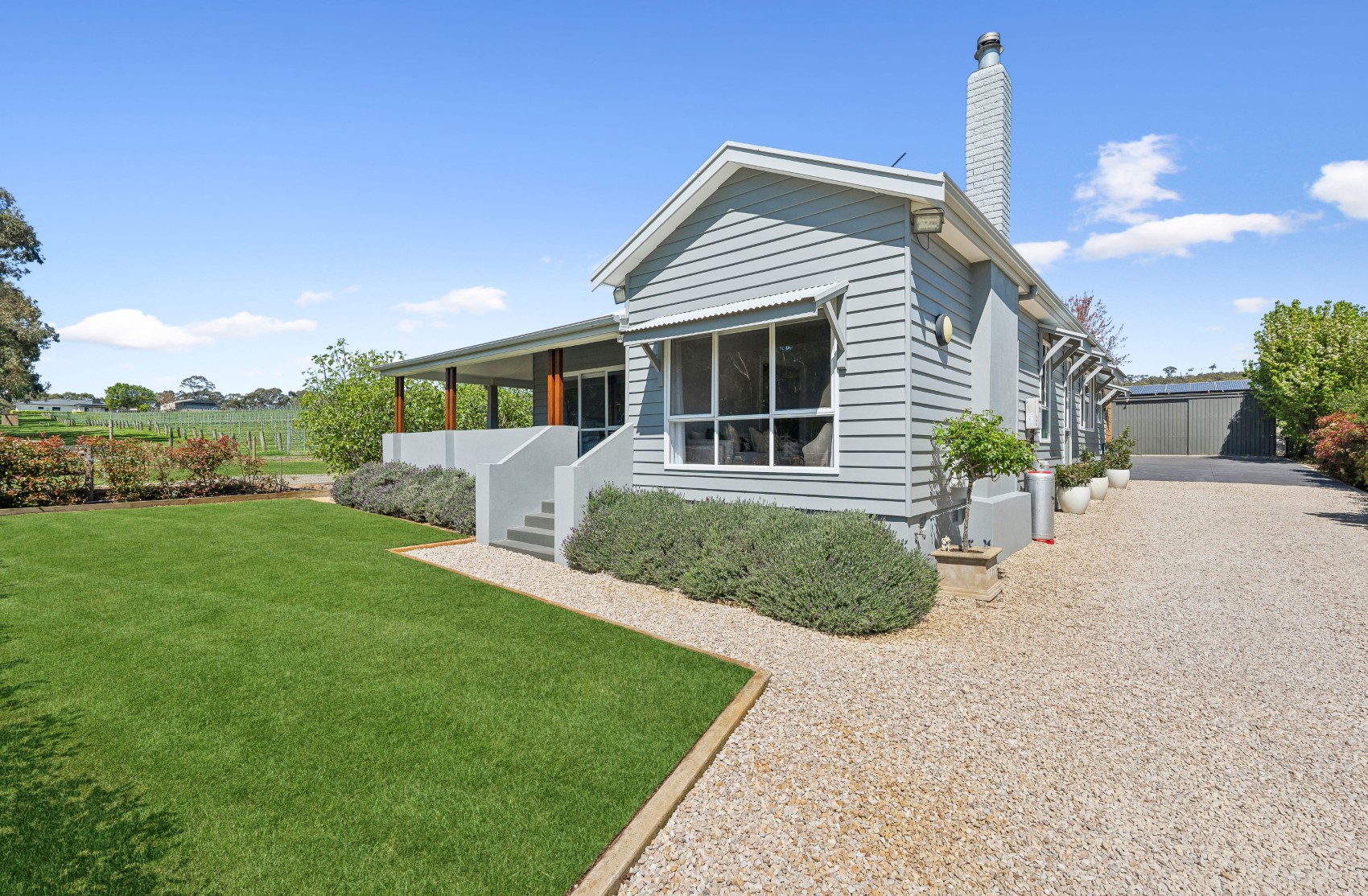 The renovated Charleston home from the drive — grey weatherboard, white chimney and verandah, with the vineyard behind