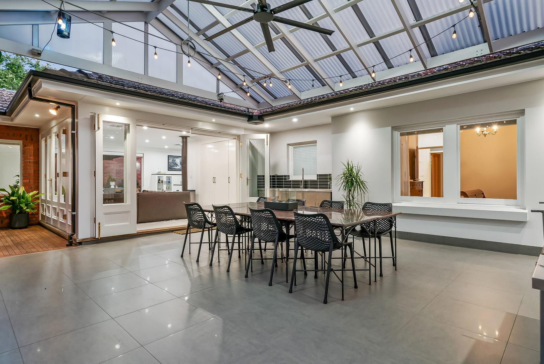 Under the Burnside pavilion — polycarbonate gable roof, fan and festoon lights over the tiled outdoor dining, outdoor kitchen behind