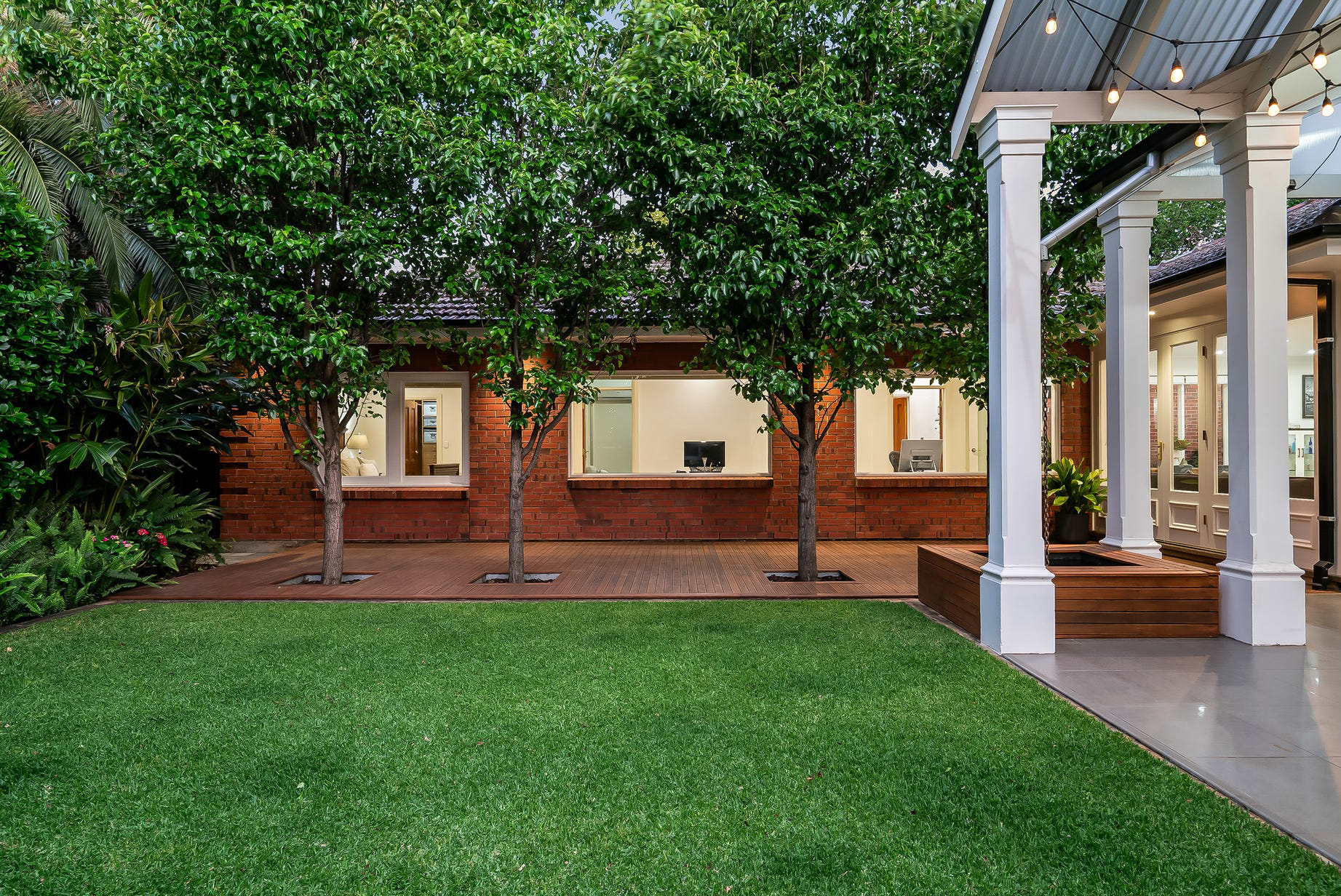Burnside courtyard with ornamental pears growing through cutouts in the new Merbau deck, red-brick home behind