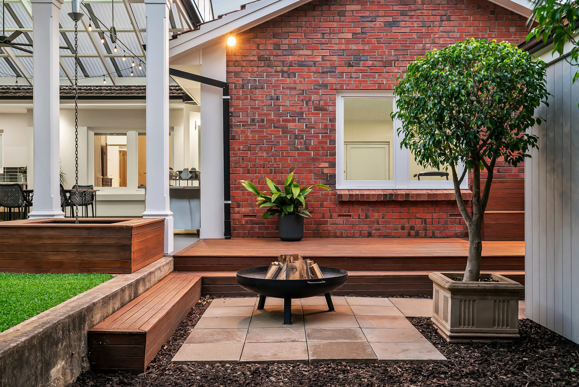 Fire pit terrace stepped down from the new Merbau deck at Burnside, timber window seat built against the red-brick wall