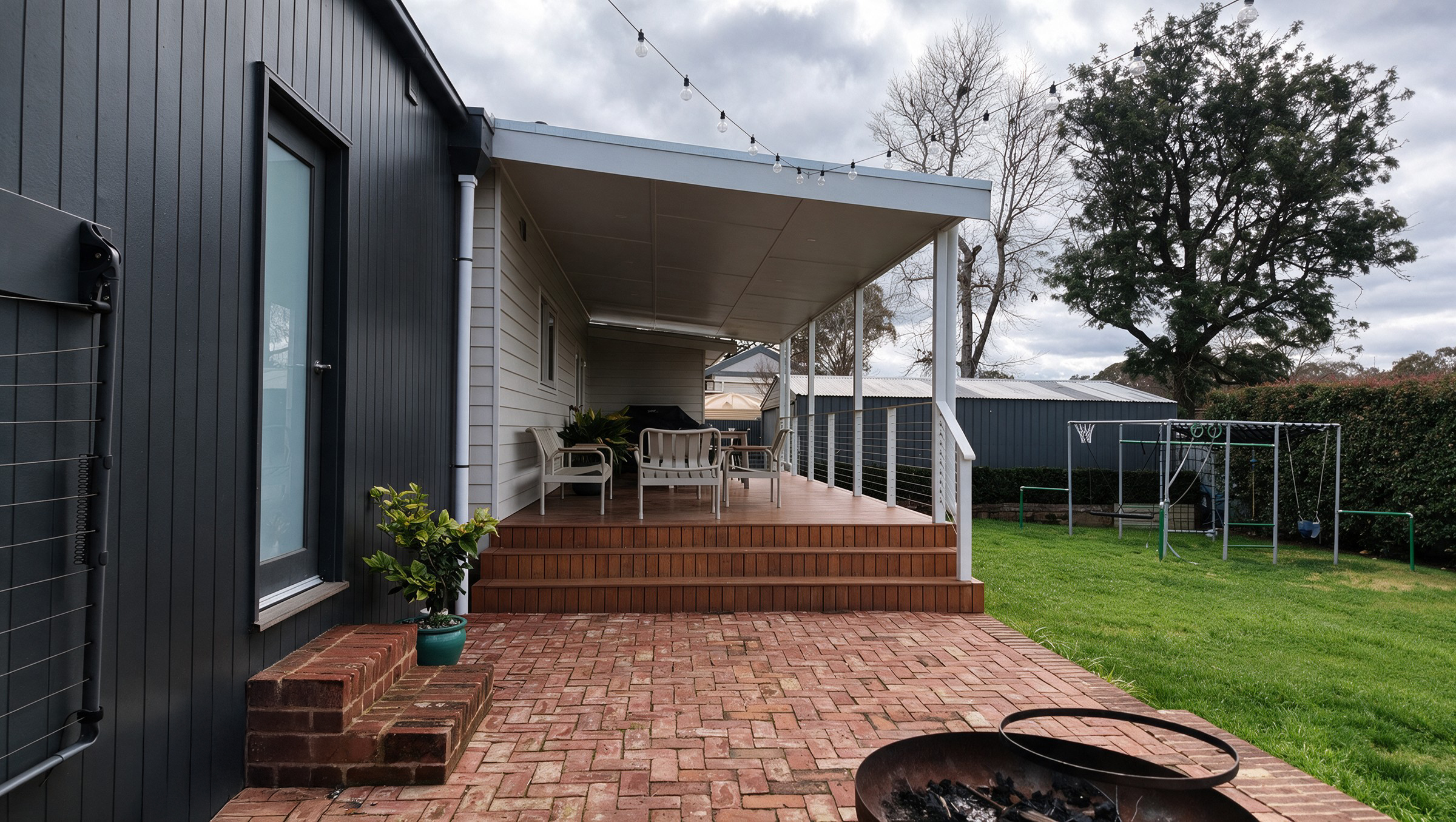 The brick terrace and fire pit looking out to the lawn, with the deck steps and verandah alongside