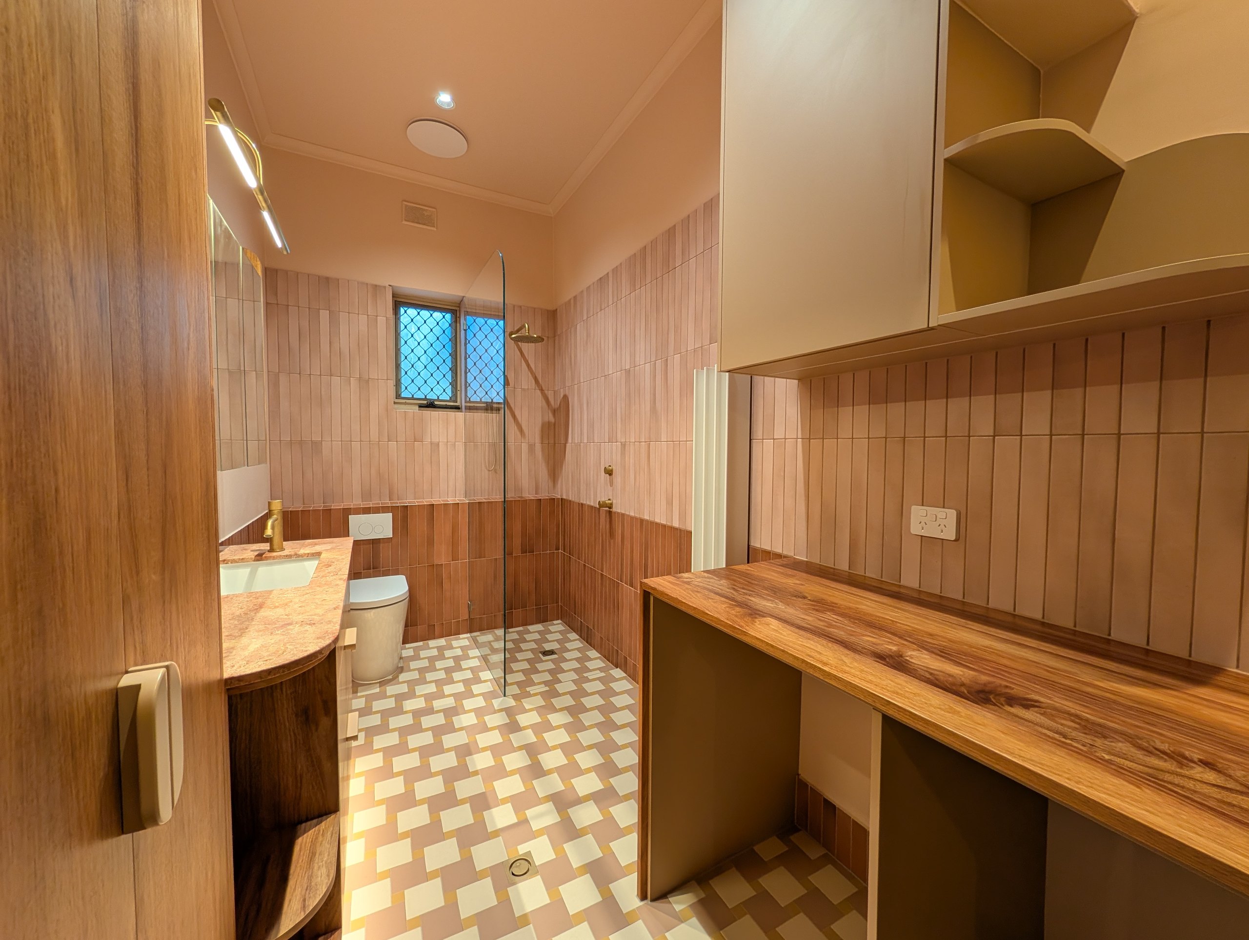 Combined bathroom and laundry: timber laundry bench on the right, vanity, toilet and walk-in shower beyond