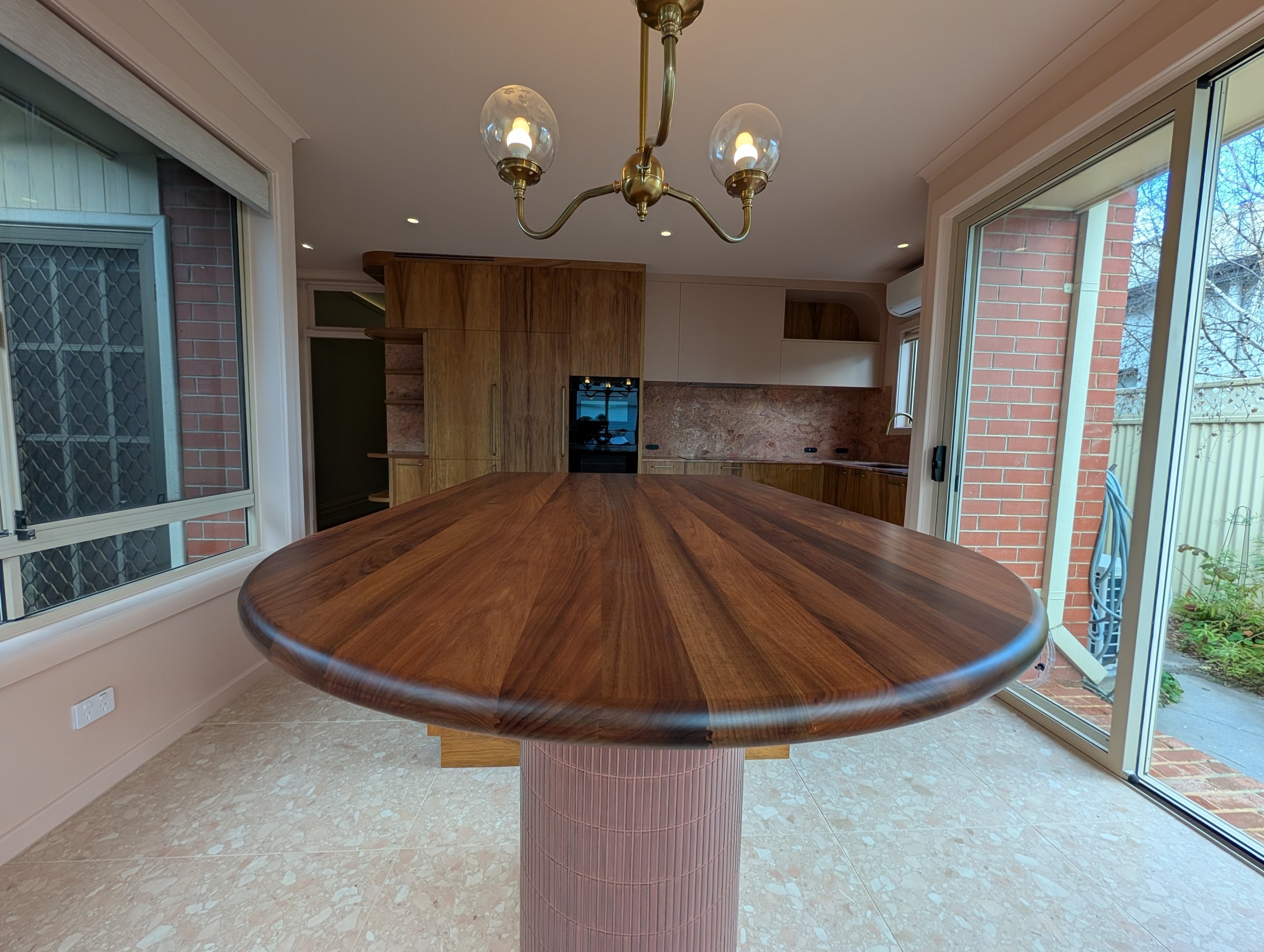 Rounded timber dining table at the end of the kitchen island, looking back to the timber and stone kitchen