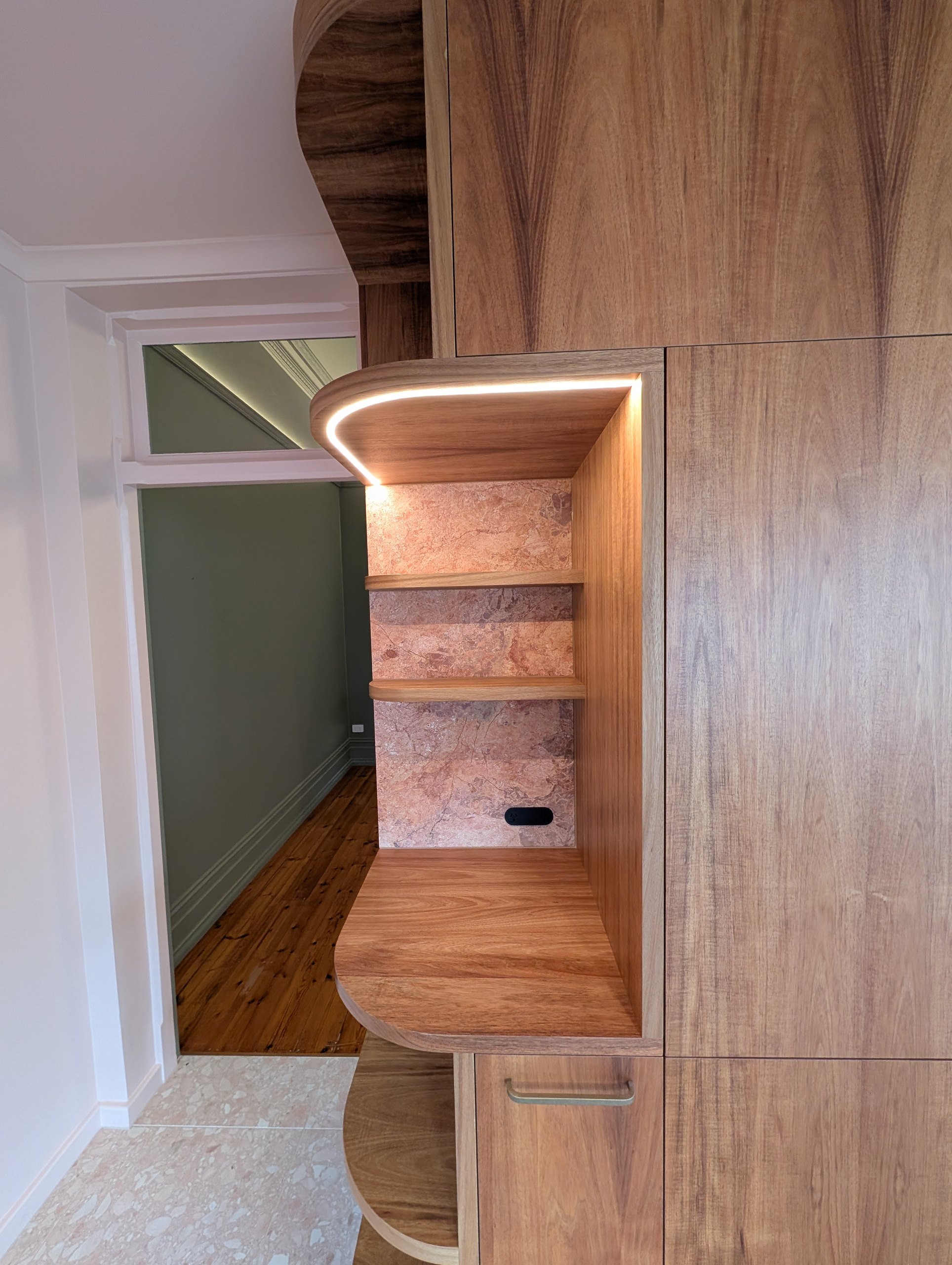 Curved timber niche at the end of the kitchen joinery, lined in stone and lit by a recessed LED strip