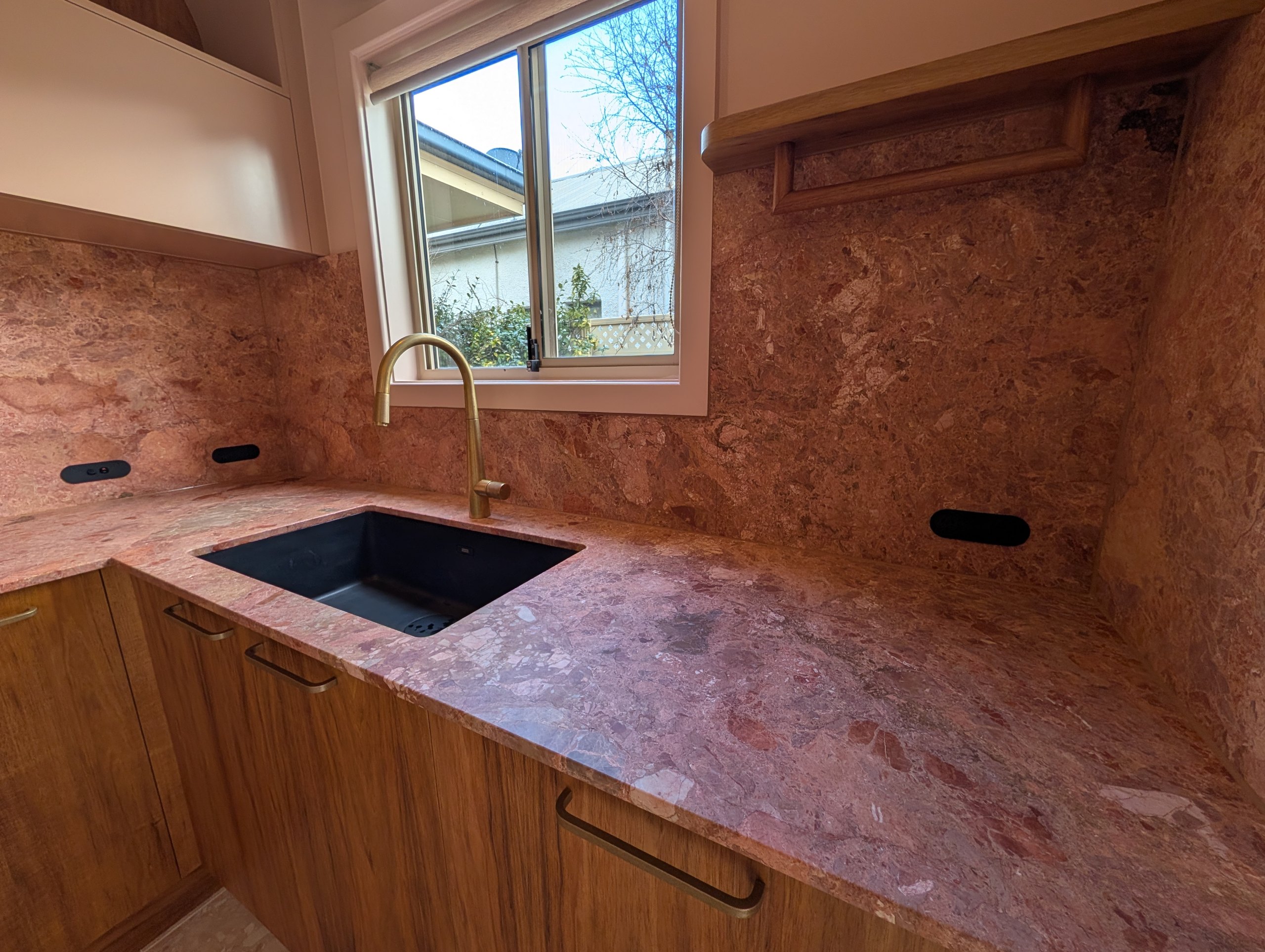 Undermount sink and brass mixer in a stone benchtop, with the same stone running up the splashback