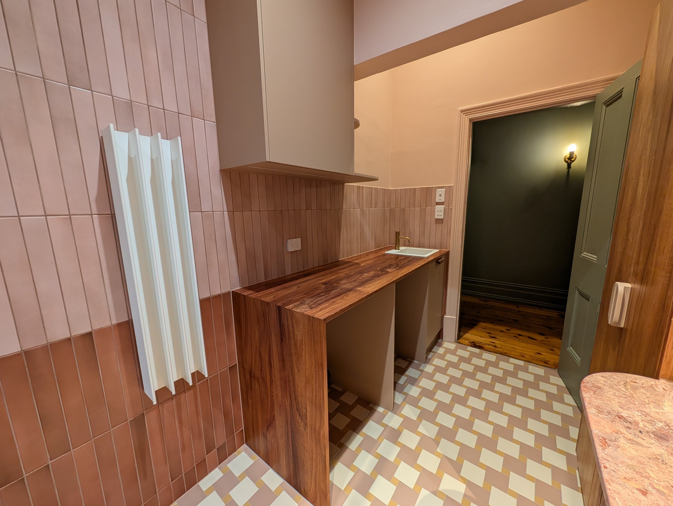 Timber laundry benchtop with a waterfall end against two-tone pink wall tiles