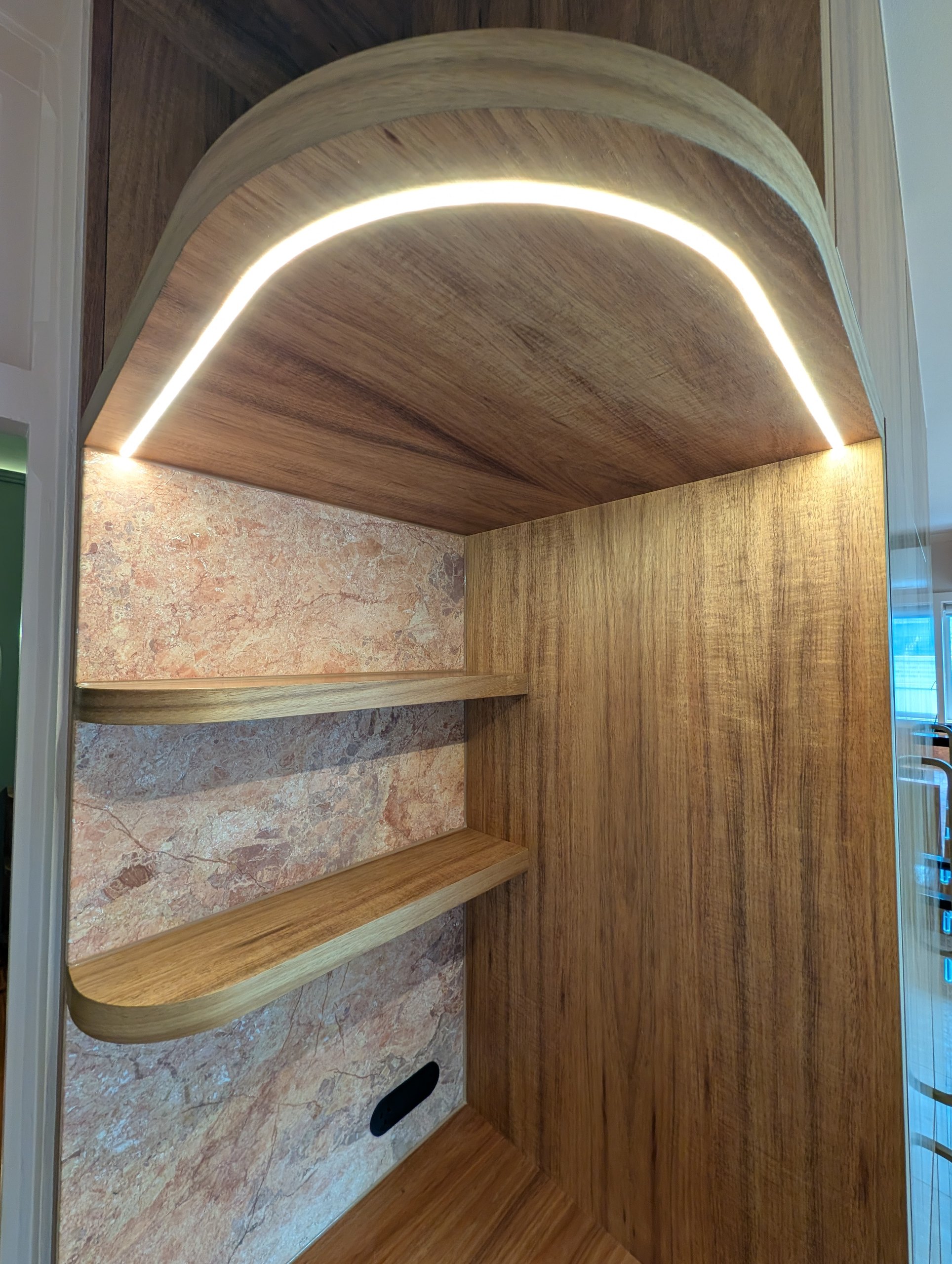 Looking up into the curved kitchen niche: recessed LED strip, timber shelves and a stone back