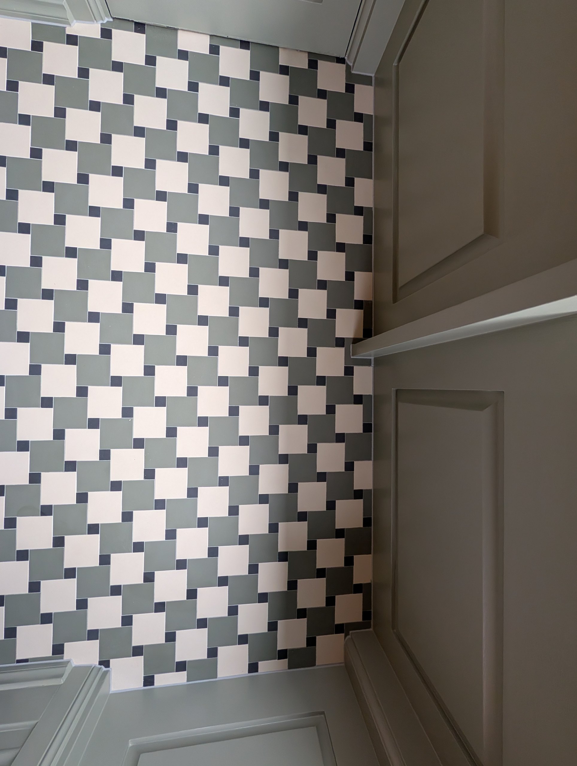 Green, blue and white pinwheel floor tiles cut in against a panelled wall, seen from above