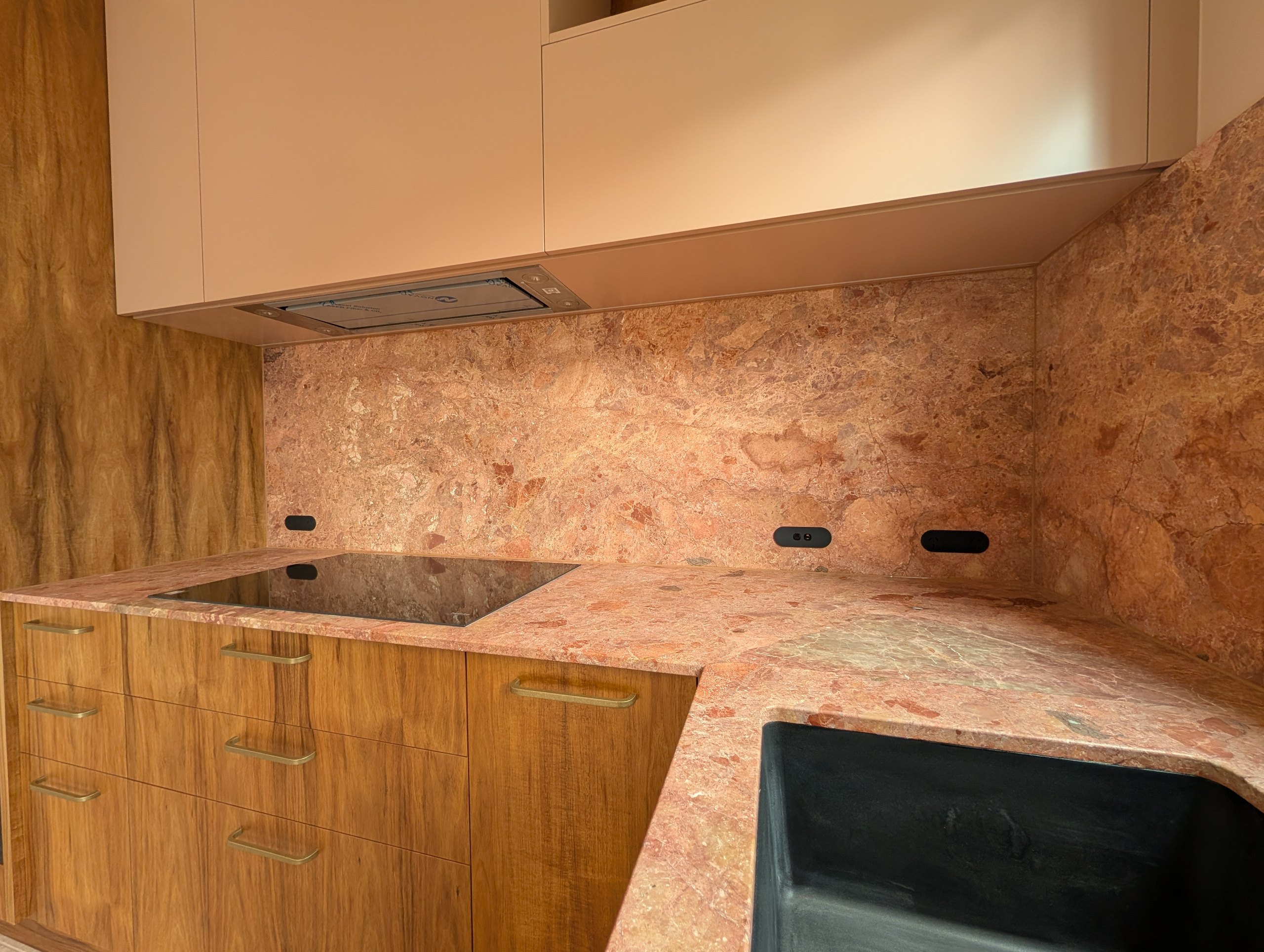 Stone benchtop and full-height stone splashback with recessed power outlets and an induction cooktop