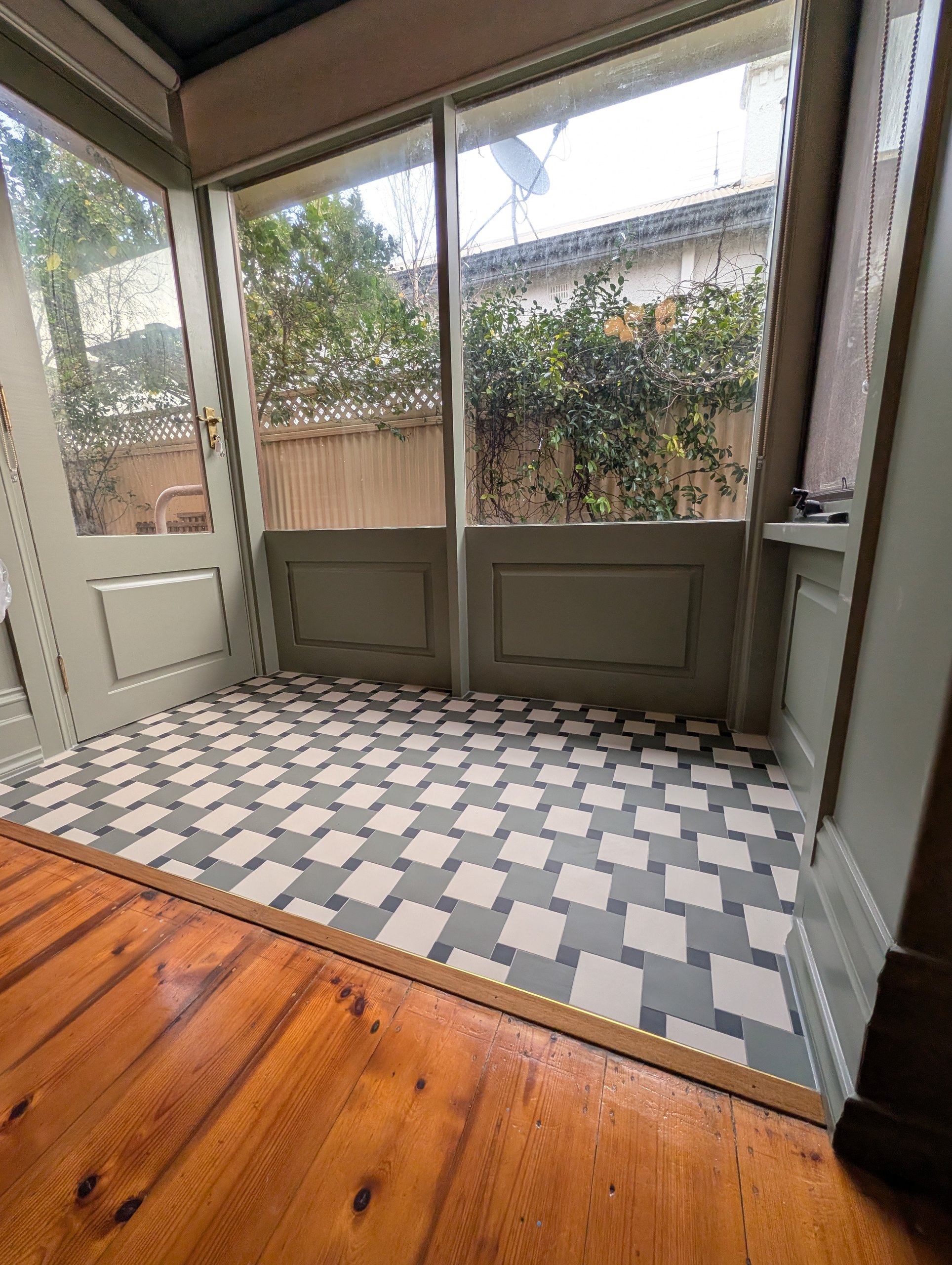 Sunroom with pinwheel tiled floor meeting the living room's timber boards at a brass threshold