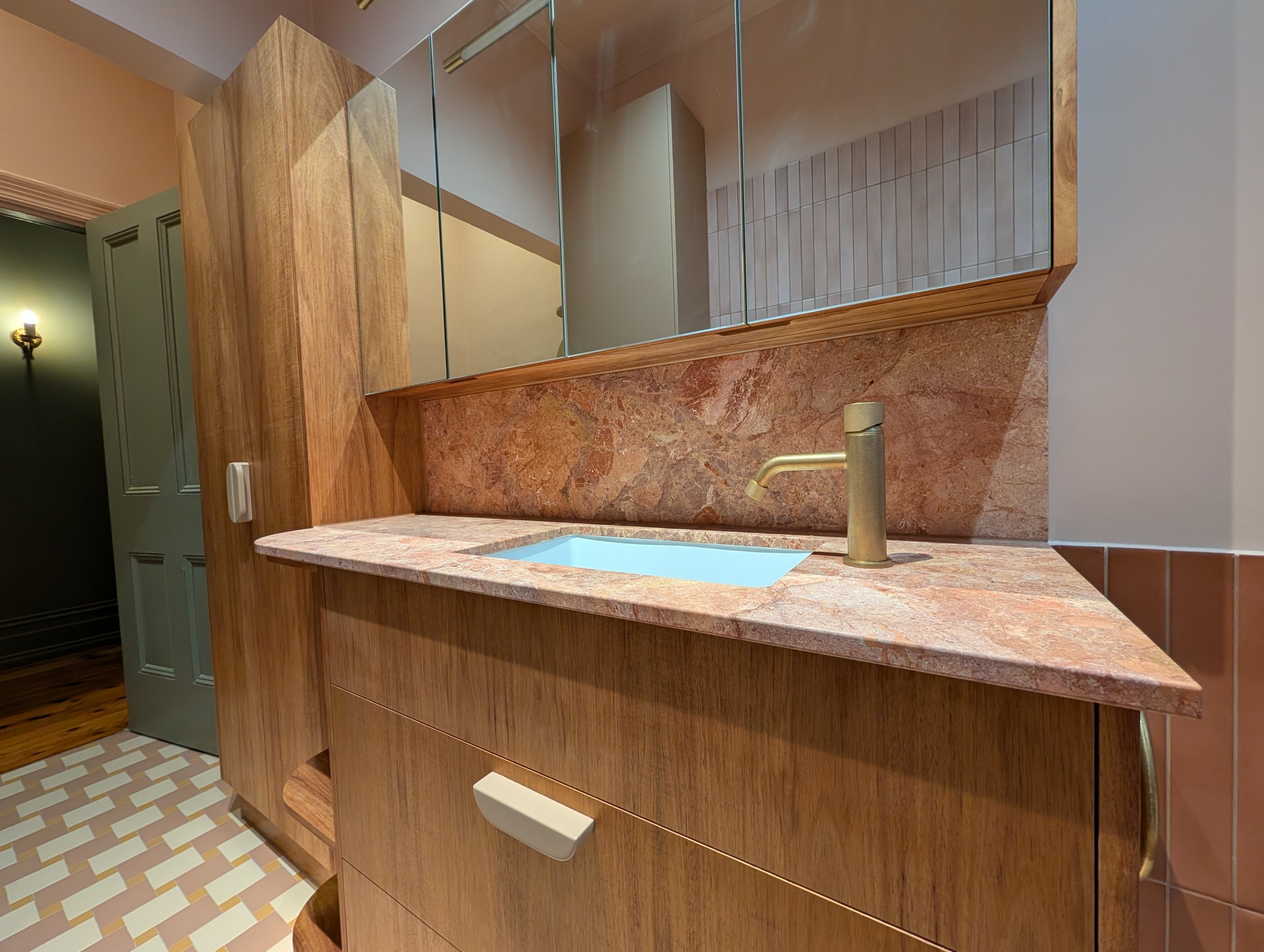 Stone vanity top and splashback with a living brass tap and a mirrored cabinet above