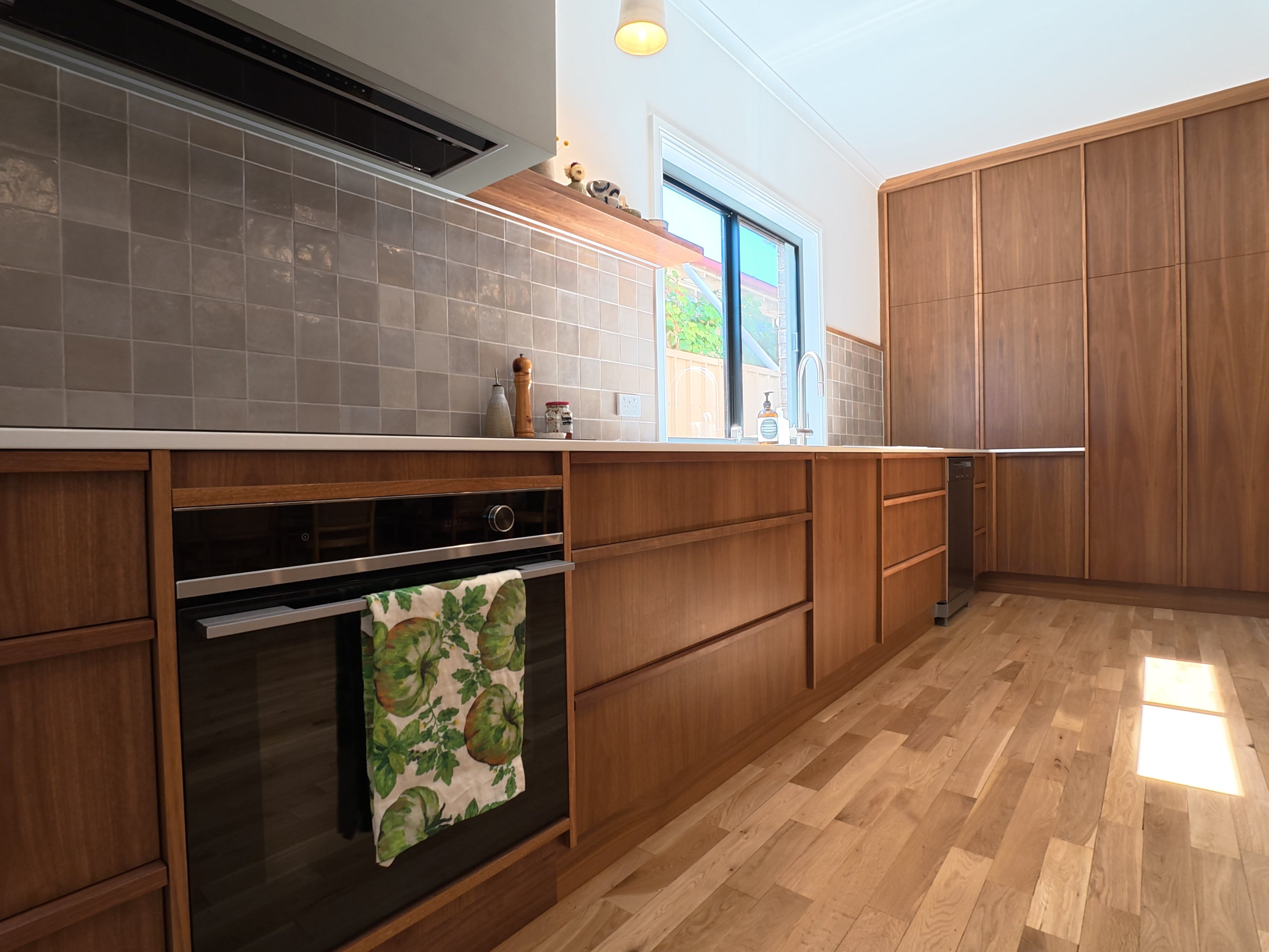 Timber kitchen bench run seen at an angle, with the rangehood, tiled splashback and the window to the yard