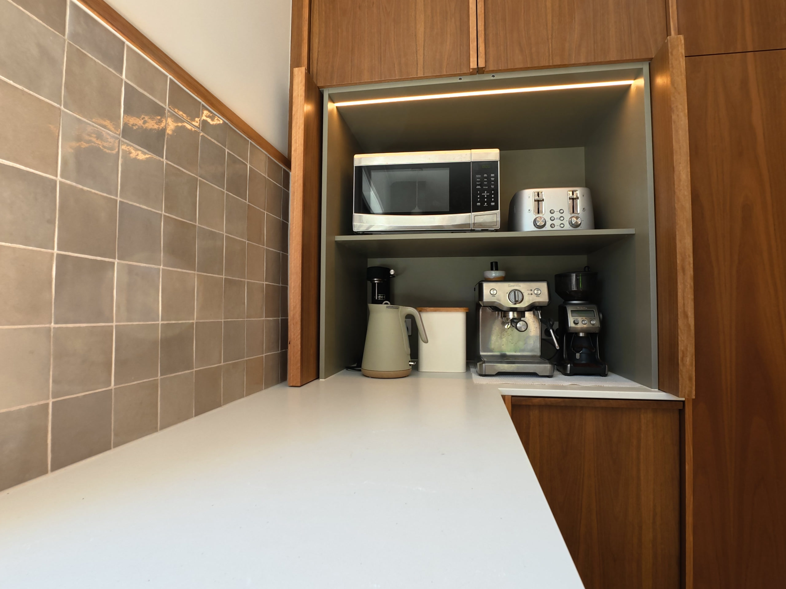 Corner cupboard open to show the coffee machine, kettle and microwave on lit shelves