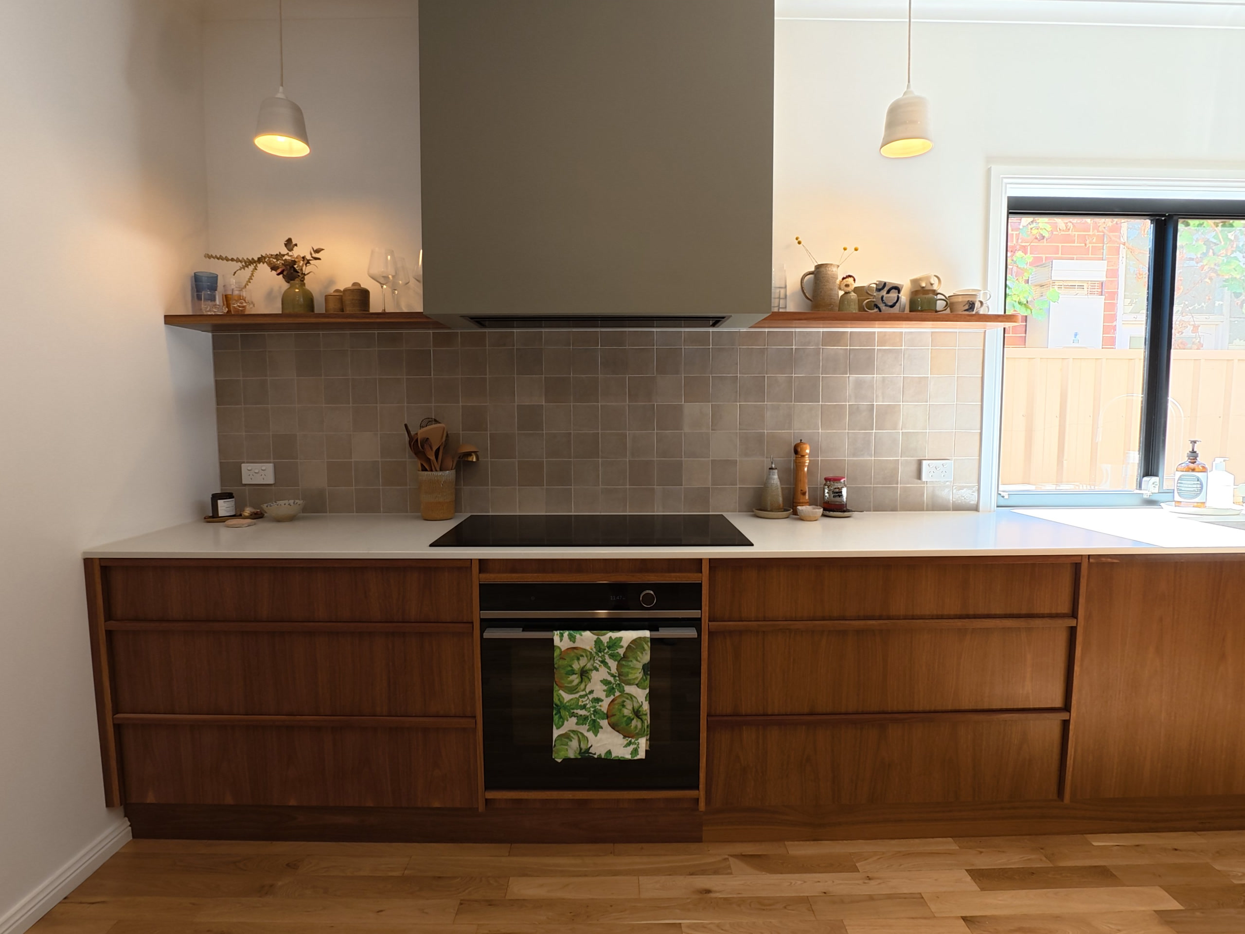 Induction cooktop and oven in the timber kitchen, with the tiled splashback and the new double-glazed window over the bench