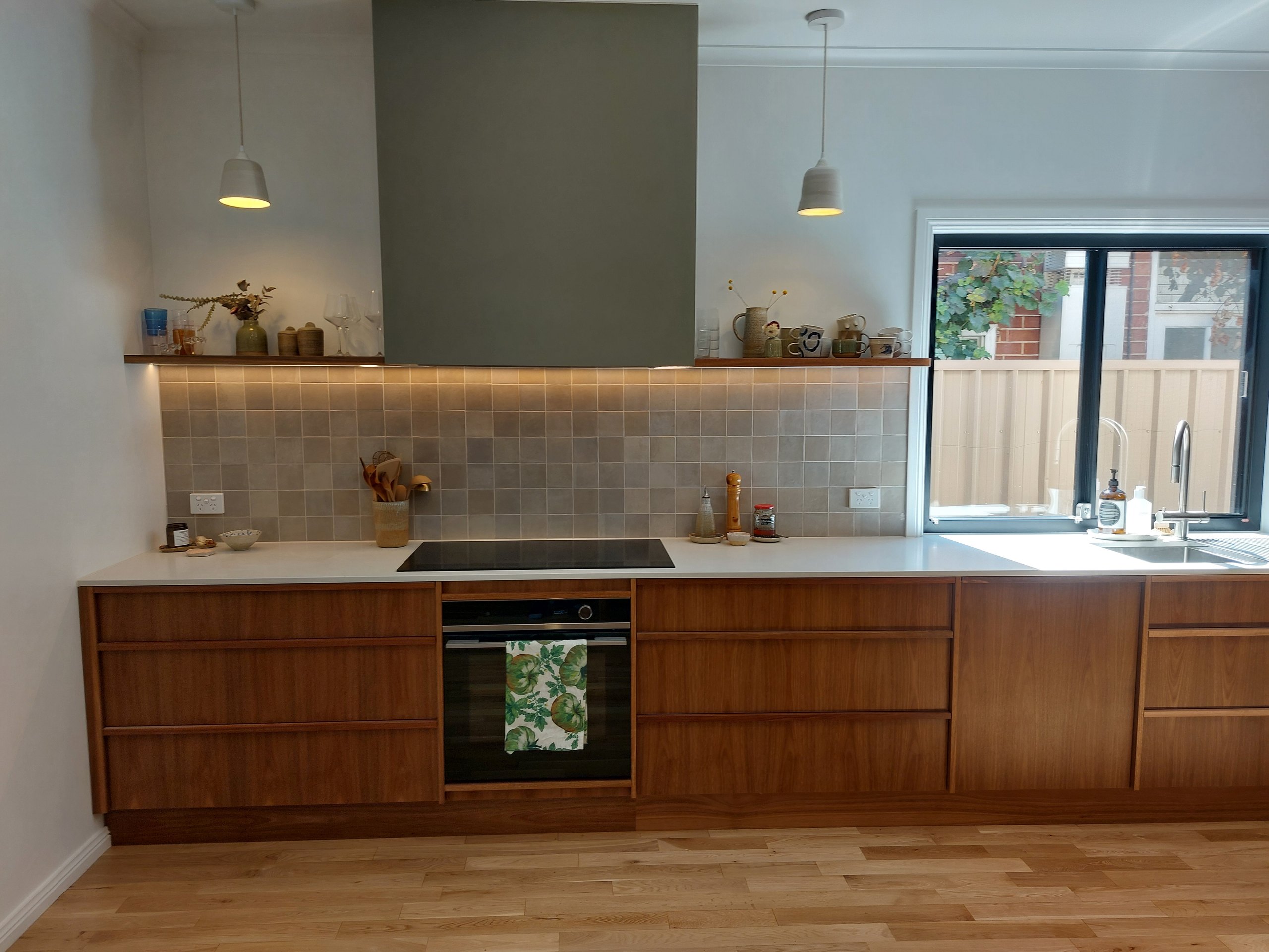 Straight-on view of the timber kitchen with the rangehood, tiled splashback, timber shelf and window
