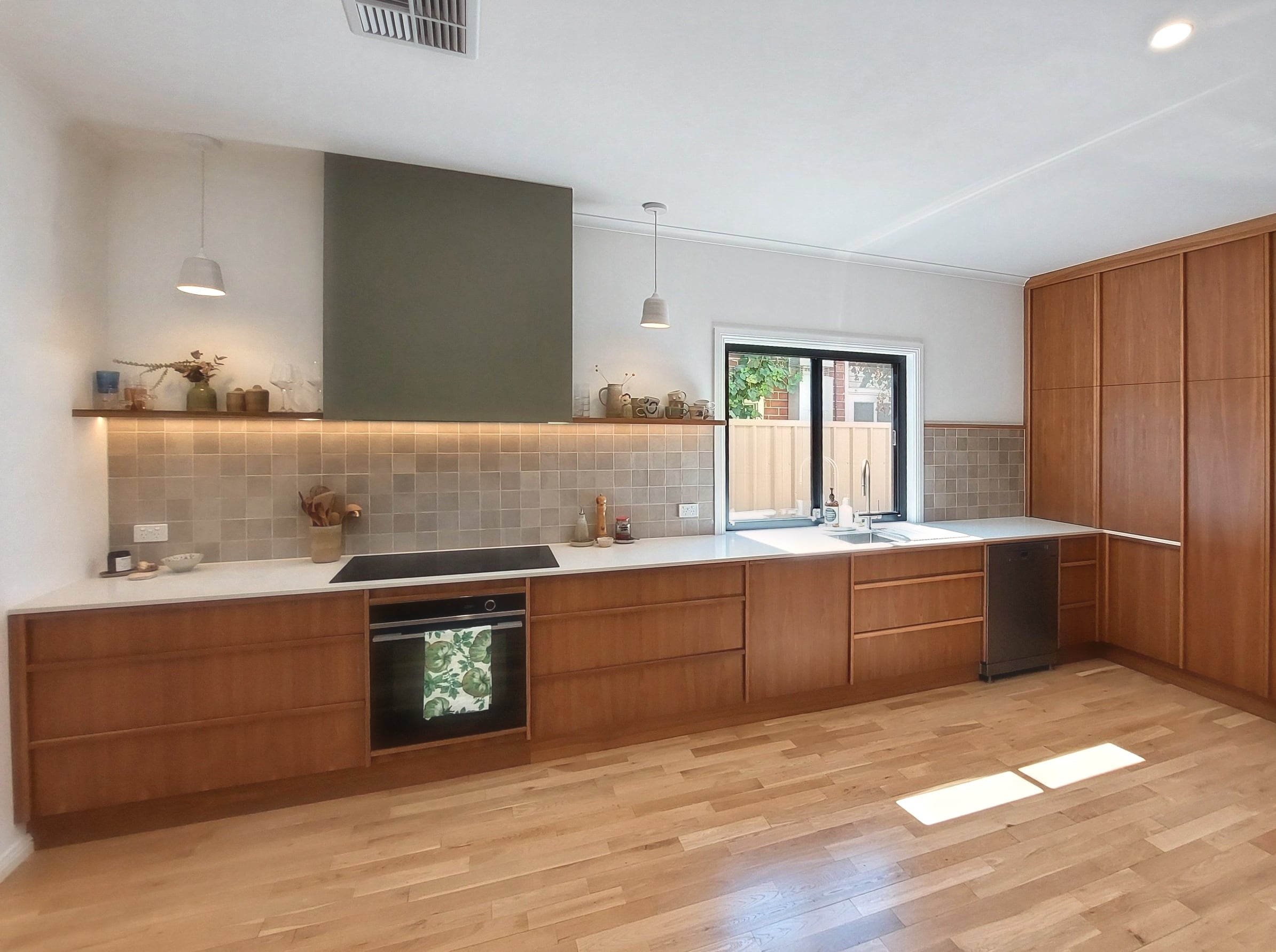 Wide view of the Kilkenny kitchen: timber bench run, rangehood, tiled splashback, pantry wall and polished timber floors