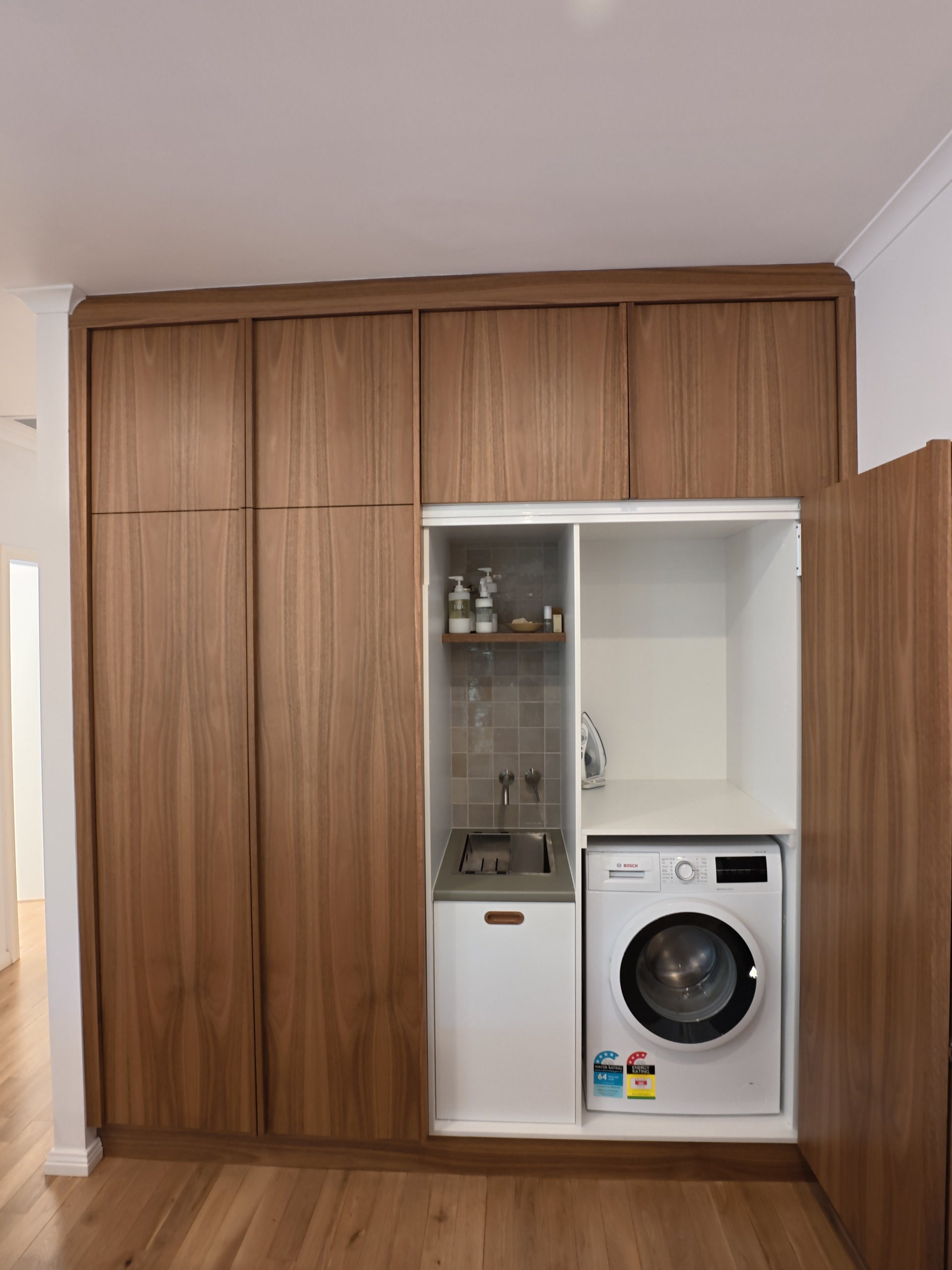 Laundry doors open in the timber joinery wall, with the washing machine and sink inside