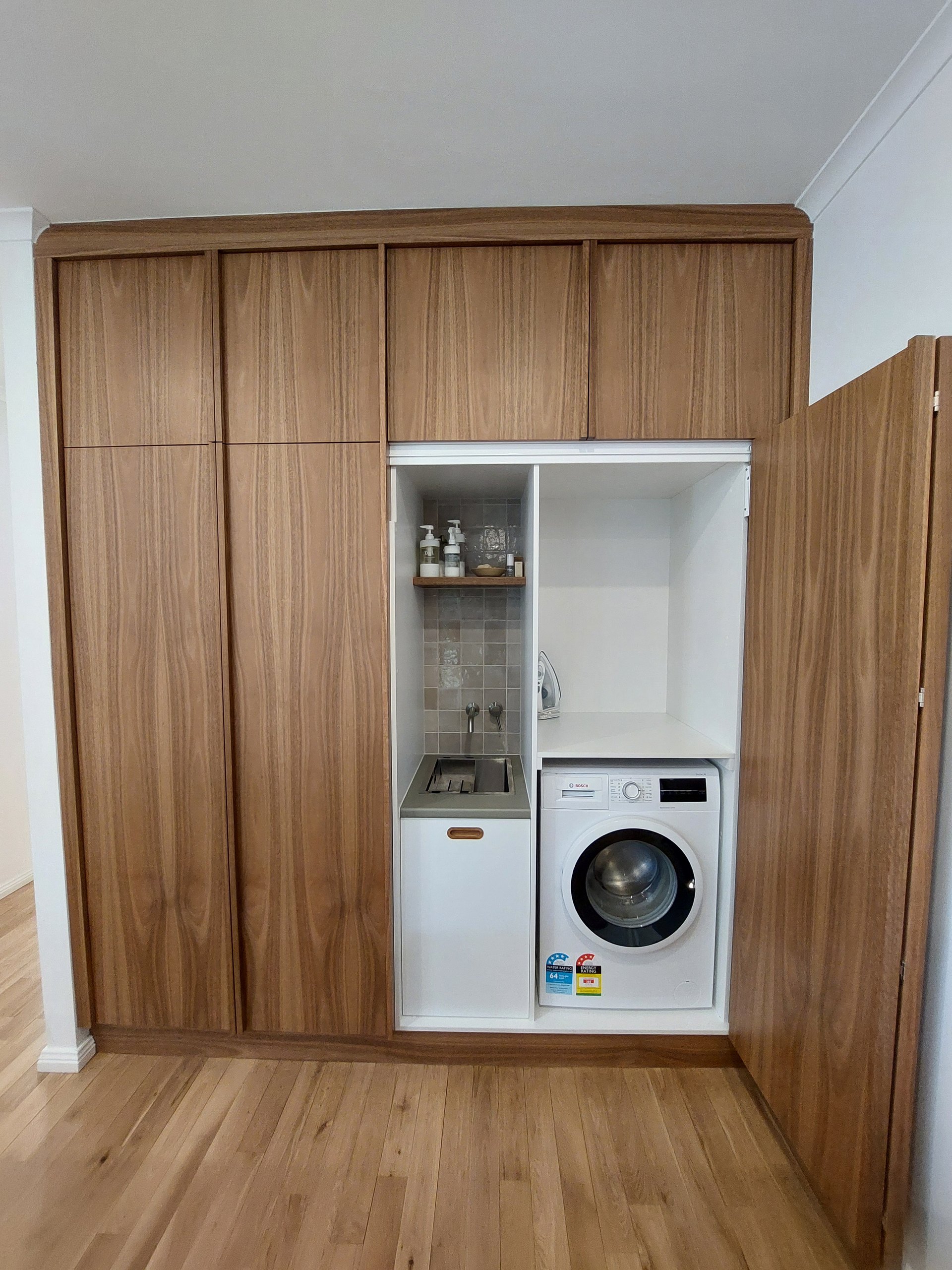 Laundry doors open to show the washing machine, sink and shelving inside the timber joinery