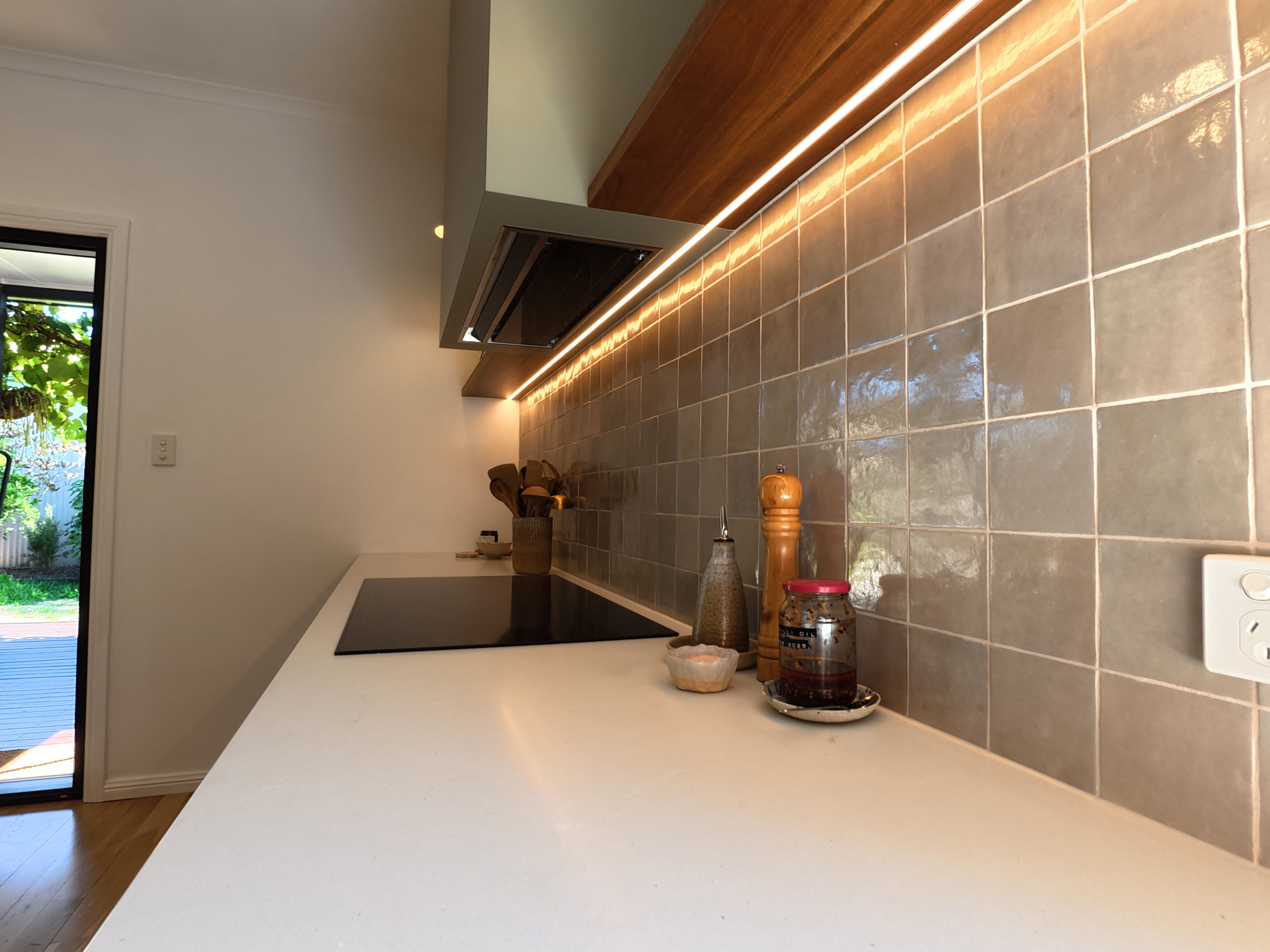 Under-cabinet LED lighting across the tiled splashback, with the sliding door to the yard beyond