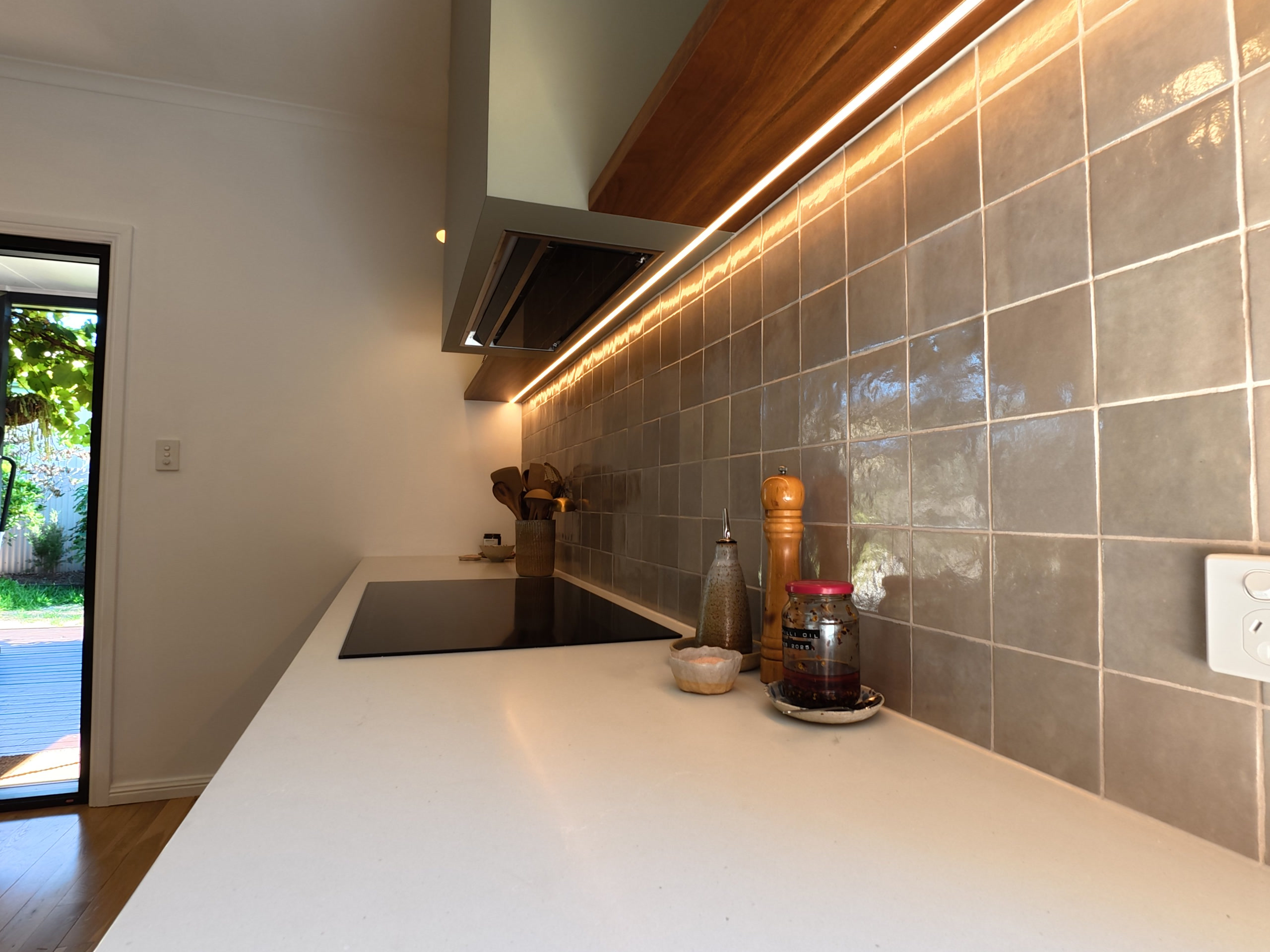 LED strip lighting under the overhead cabinets lighting the tiled splashback and benchtop